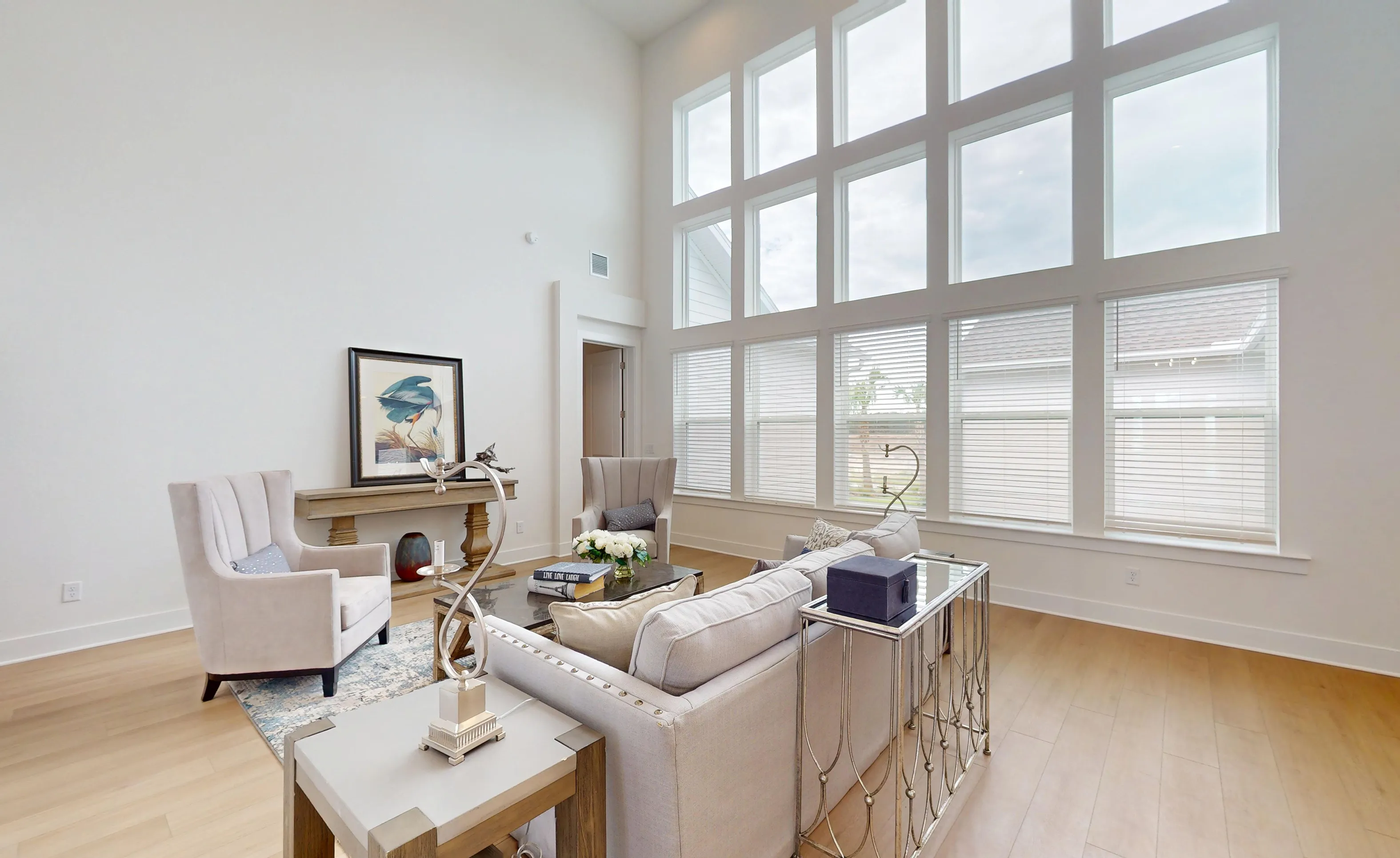 Living room of the Braddock plan with soaring ceilings, a wall of stacked windows, light wood floors, and neutral furniture.