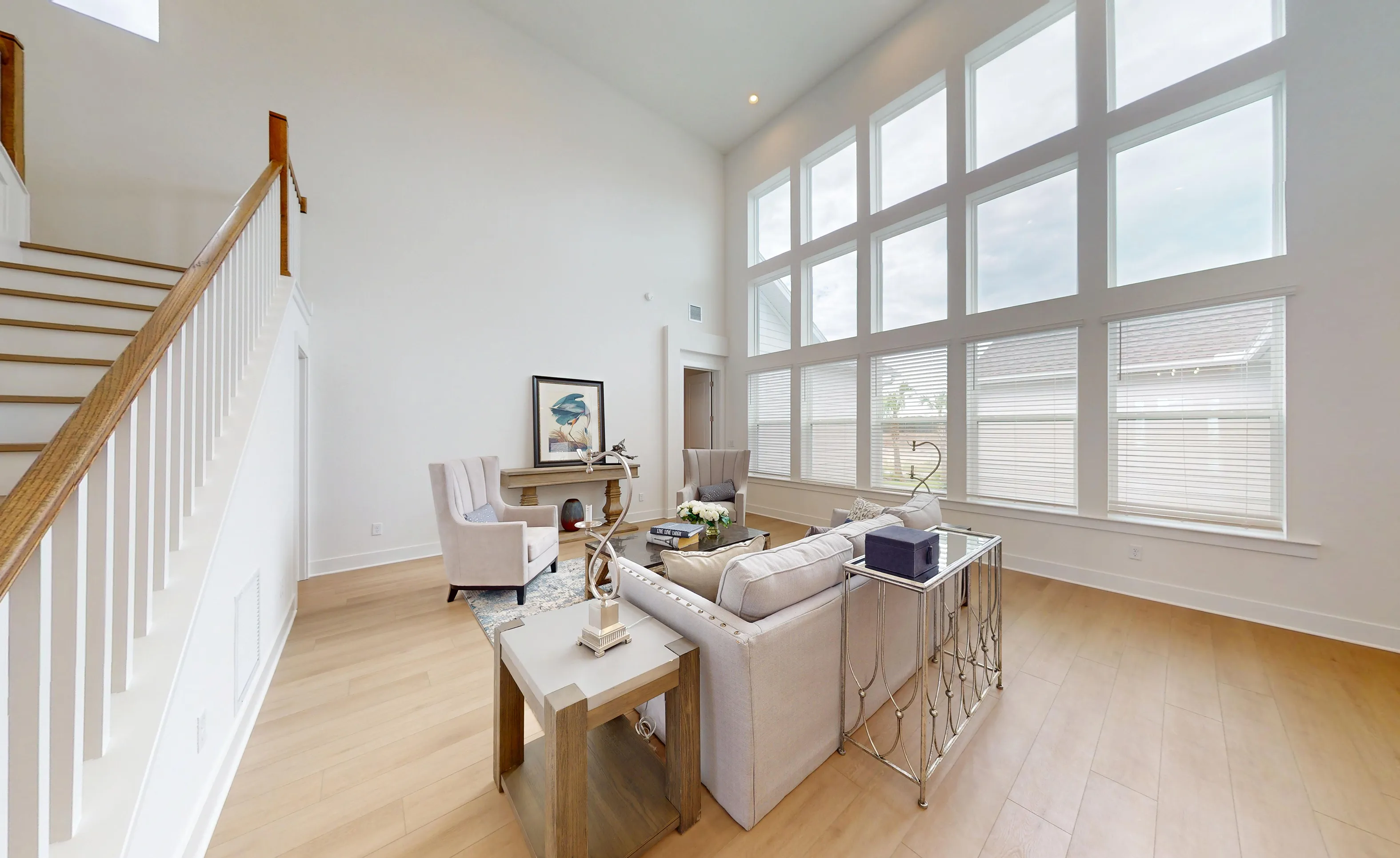 Braddock living room with two-story windows, light wood floors, and an adjacent staircase with a wood railing.