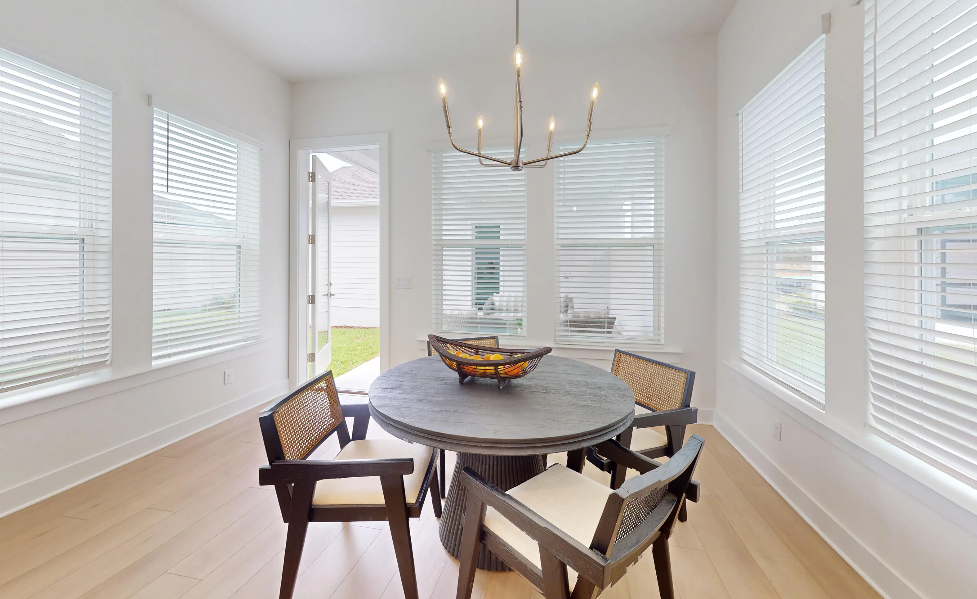 Bright breakfast nook in the Braddock plan featuring light wood floors, a round dark table, and multiple windows with blinds.