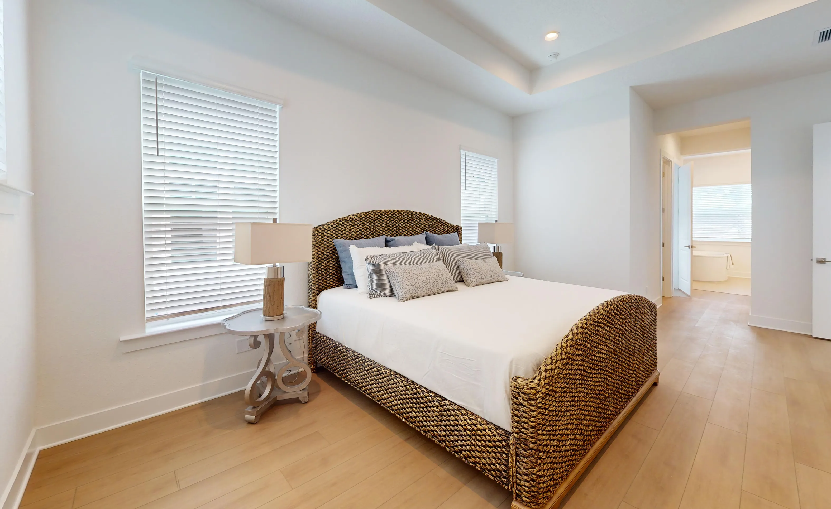 Primary bedroom in the Braddock plan with light wood flooring, white walls, a coffered ceiling, and a woven-textured bed frame.