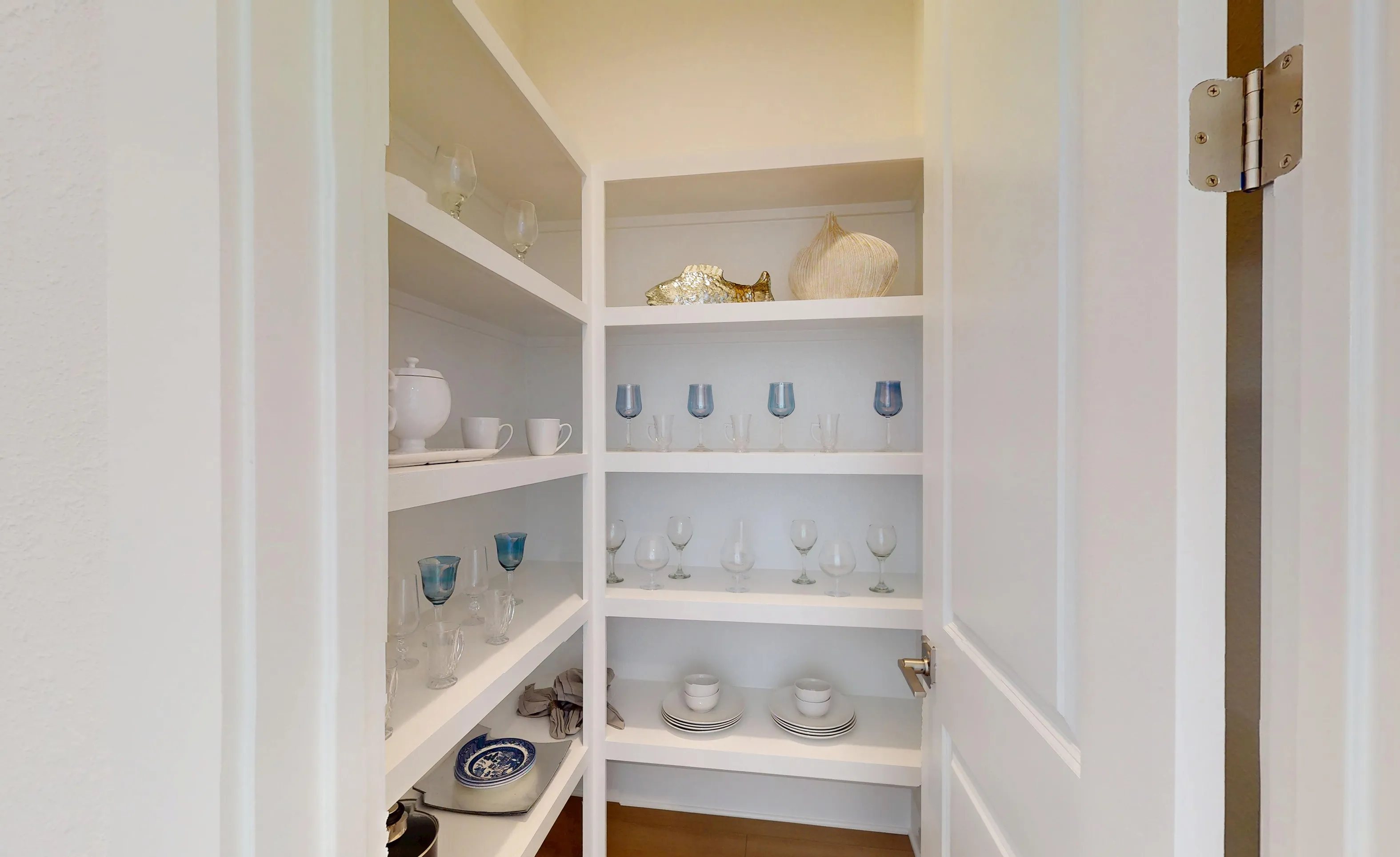 White walk-in kitchen pantry in the Braddock plan at Seven Pines with corner shelving displaying glassware and dishes.