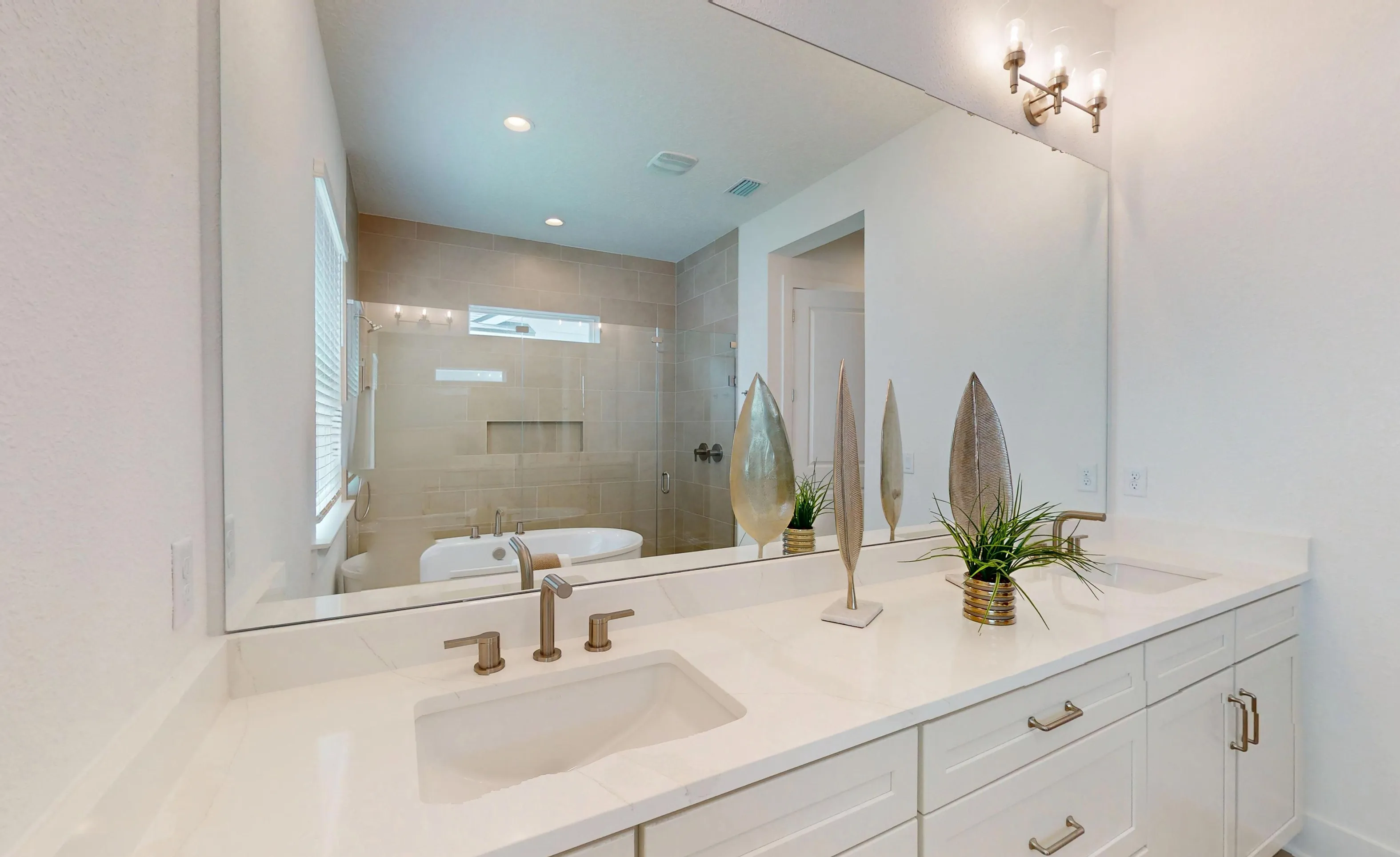 Primary bath in the Braddock plan with dual white vanity, quartz countertop, large mirror, and glass-enclosed shower/tub area.
