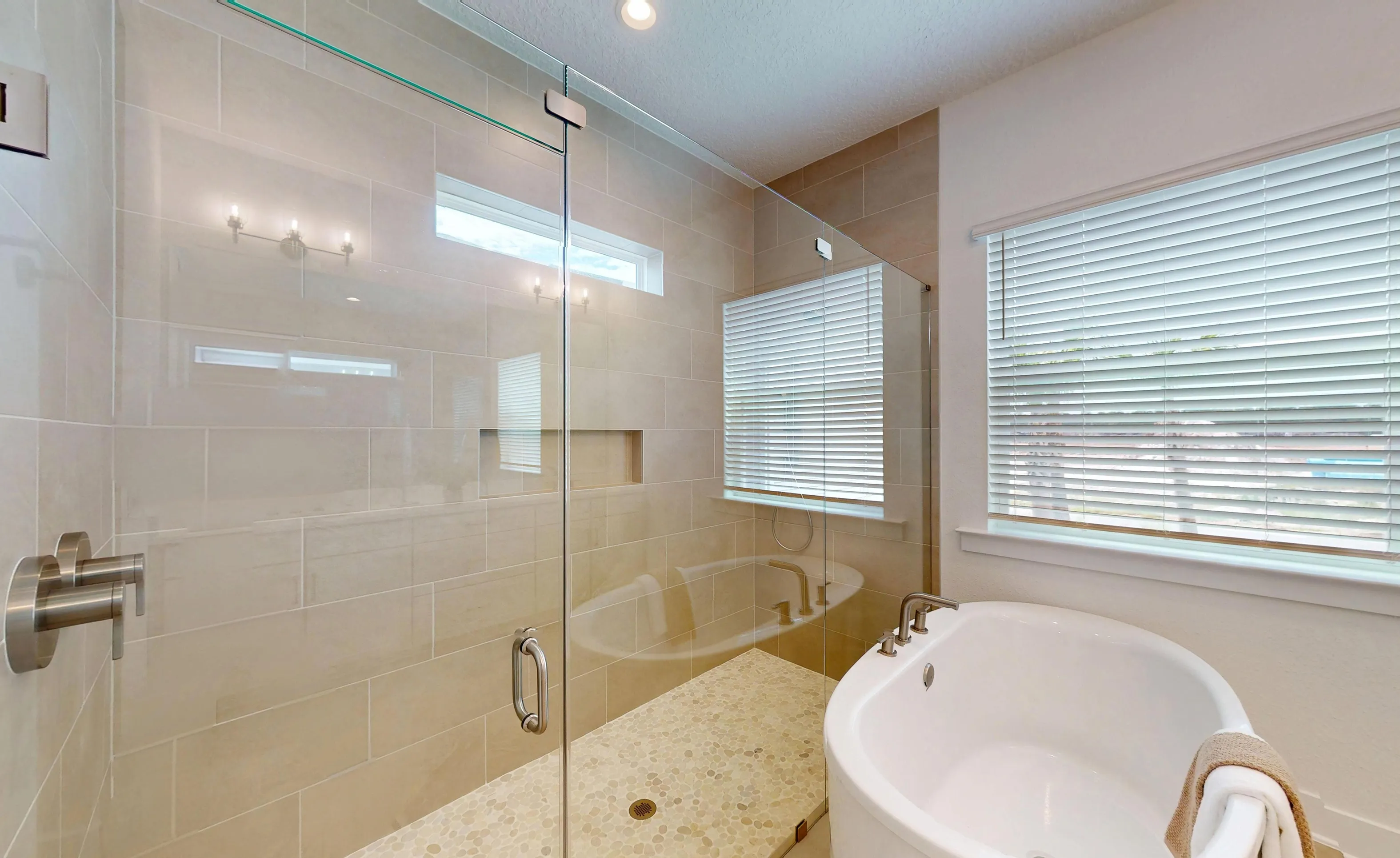 Primary bath of the Braddock plan featuring a glass-enclosed walk-in shower with beige tile, a niche, and a soaking tub.