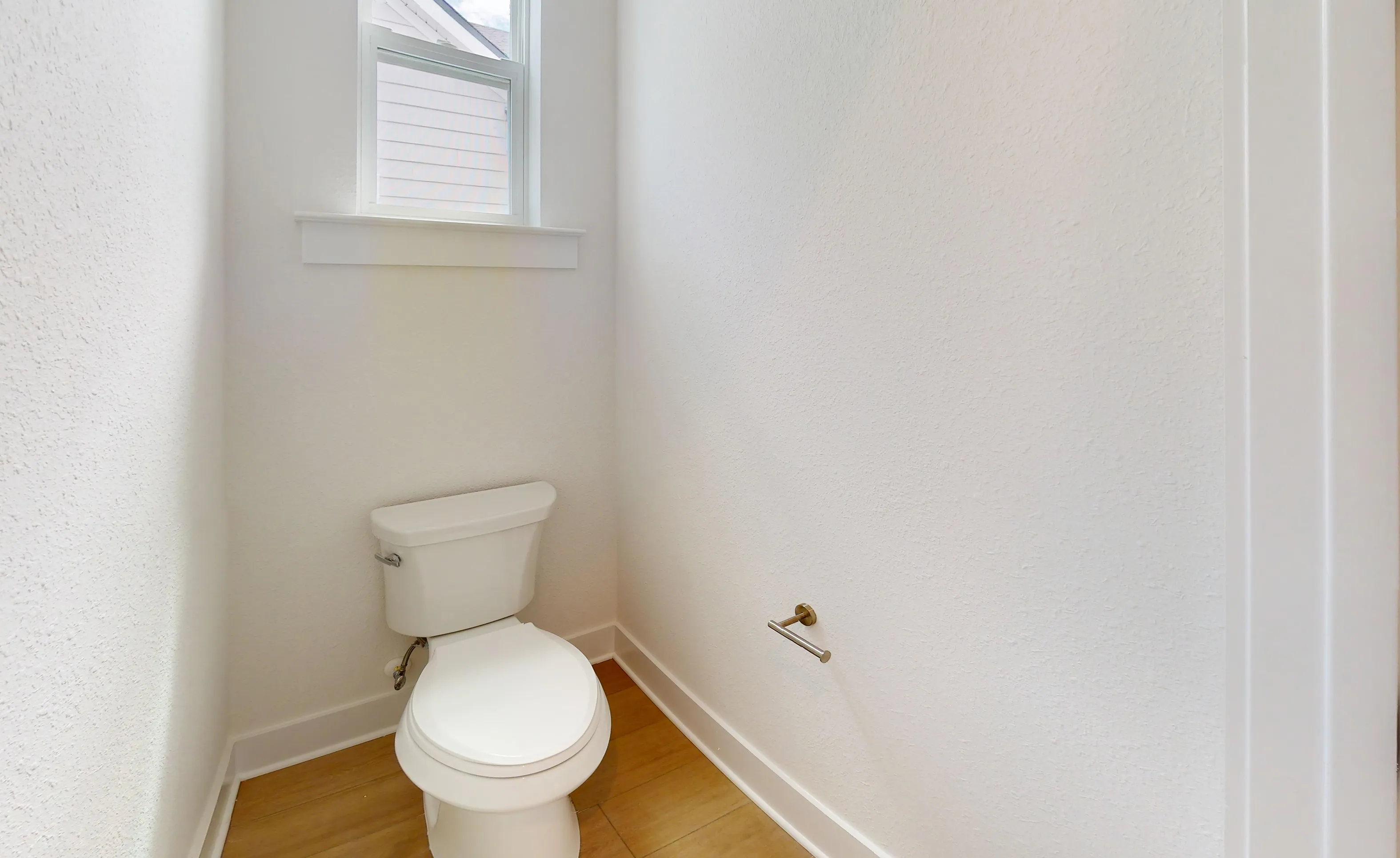 Powder room in the Braddock plan with white walls, wood-look flooring, a window, and a toilet.