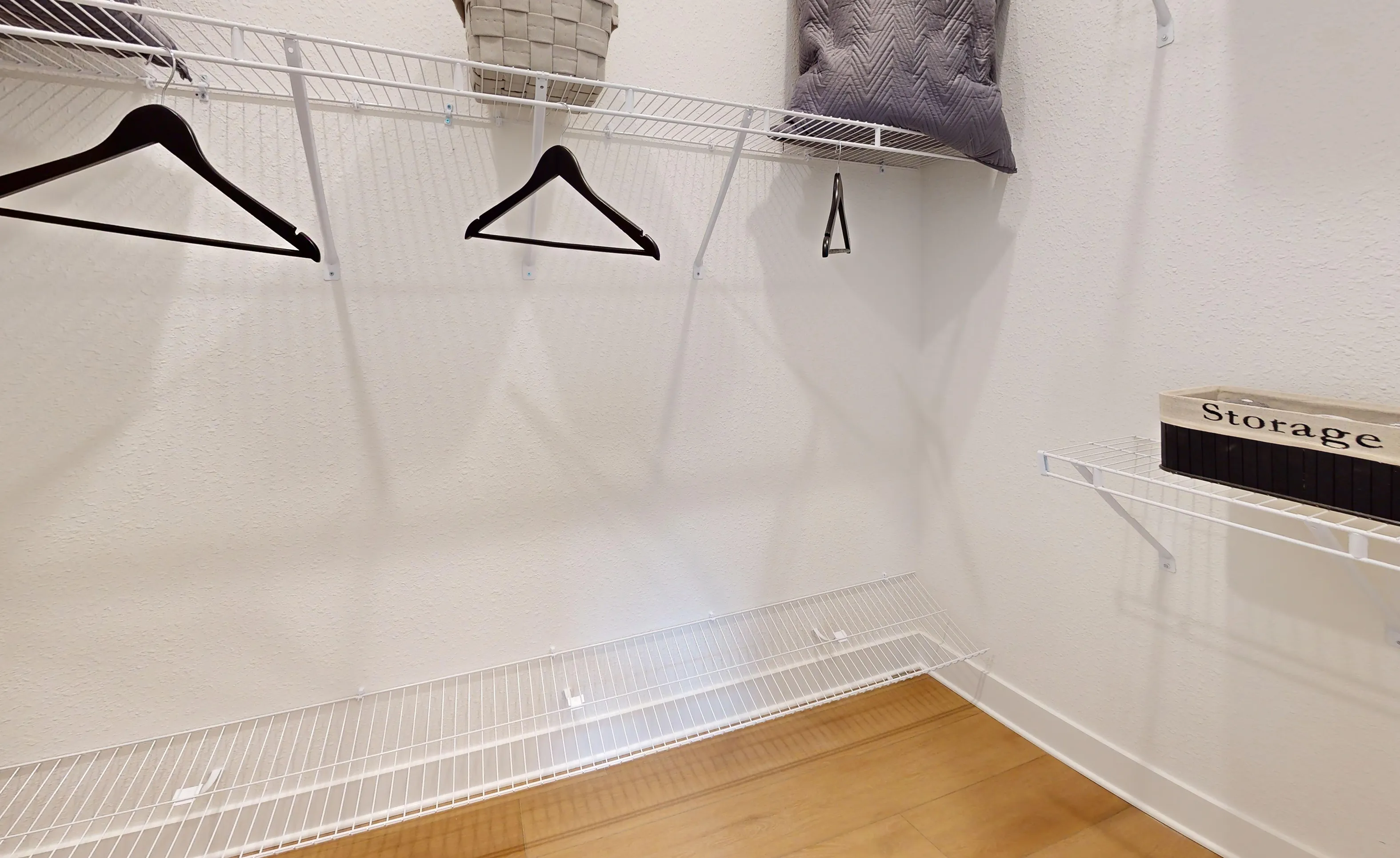 Walk-in closet in the Braddock plan with white wire shelving, black clothes hangers, and light wood-look flooring.