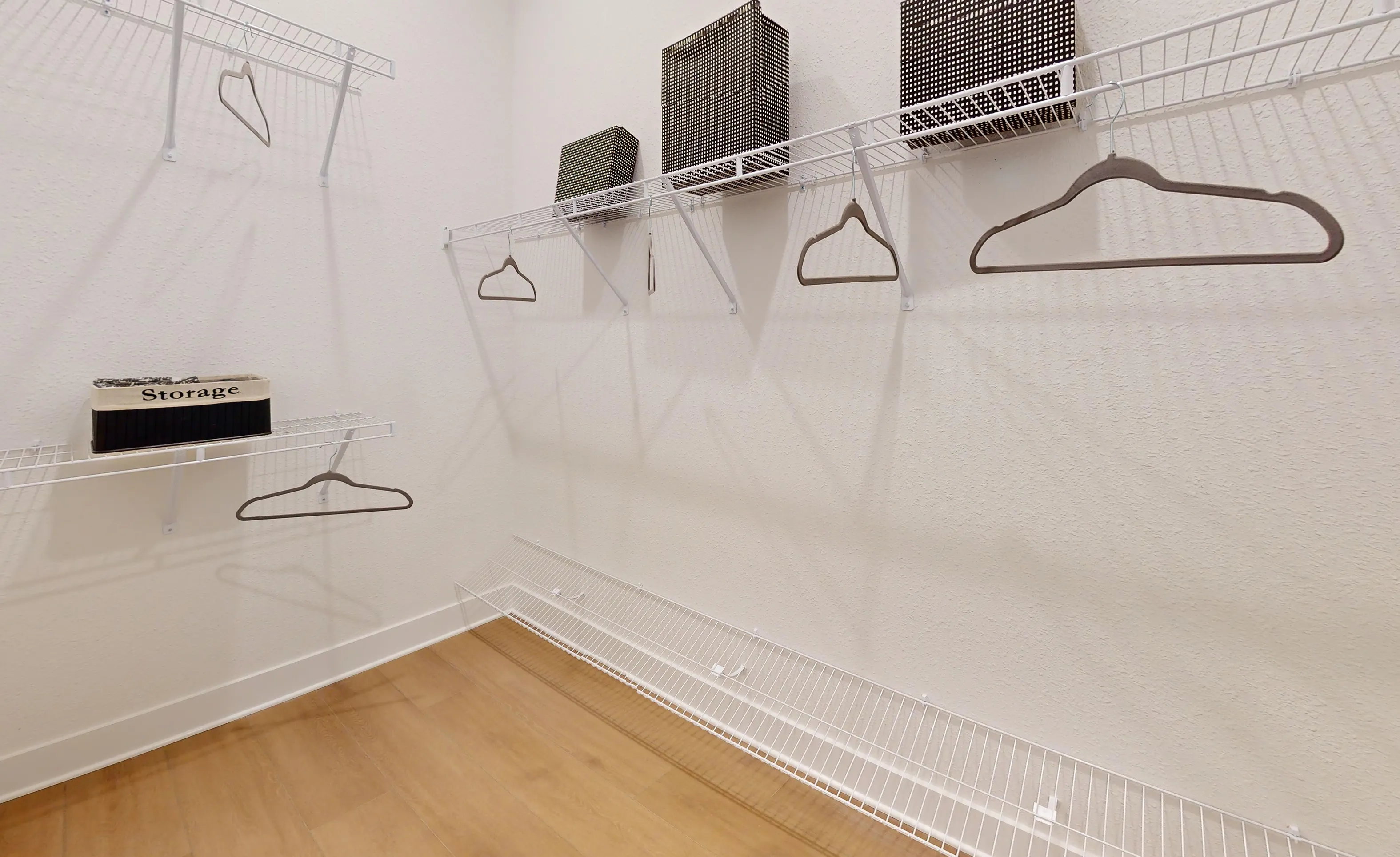 Walk-in closet in the Braddock home plan featuring white wire shelving, wall-mounted racks, and wood-look flooring.
