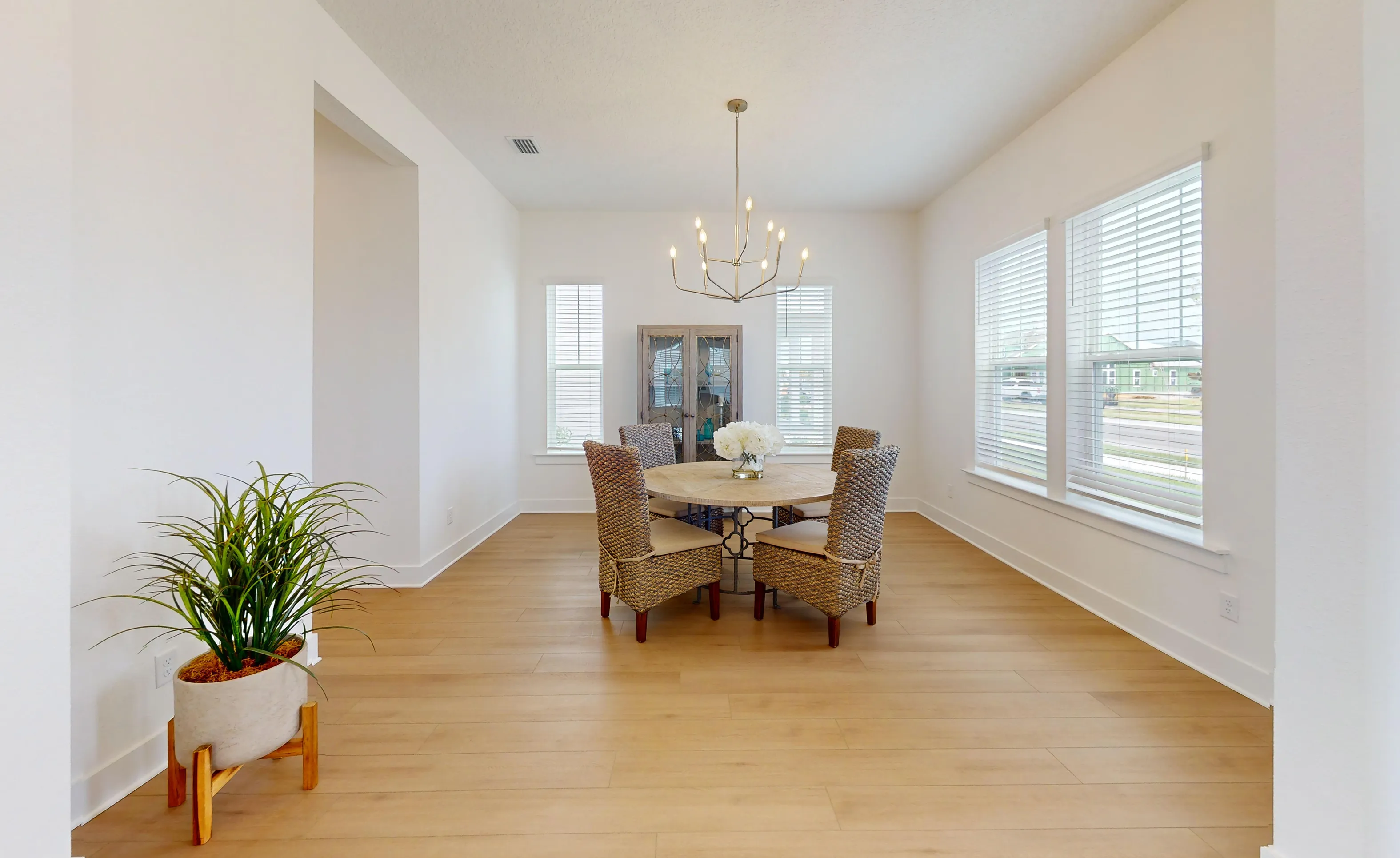 Bright dining room in the Braddock plan with light wood flooring, a central chandelier, and a round wooden table with chairs.