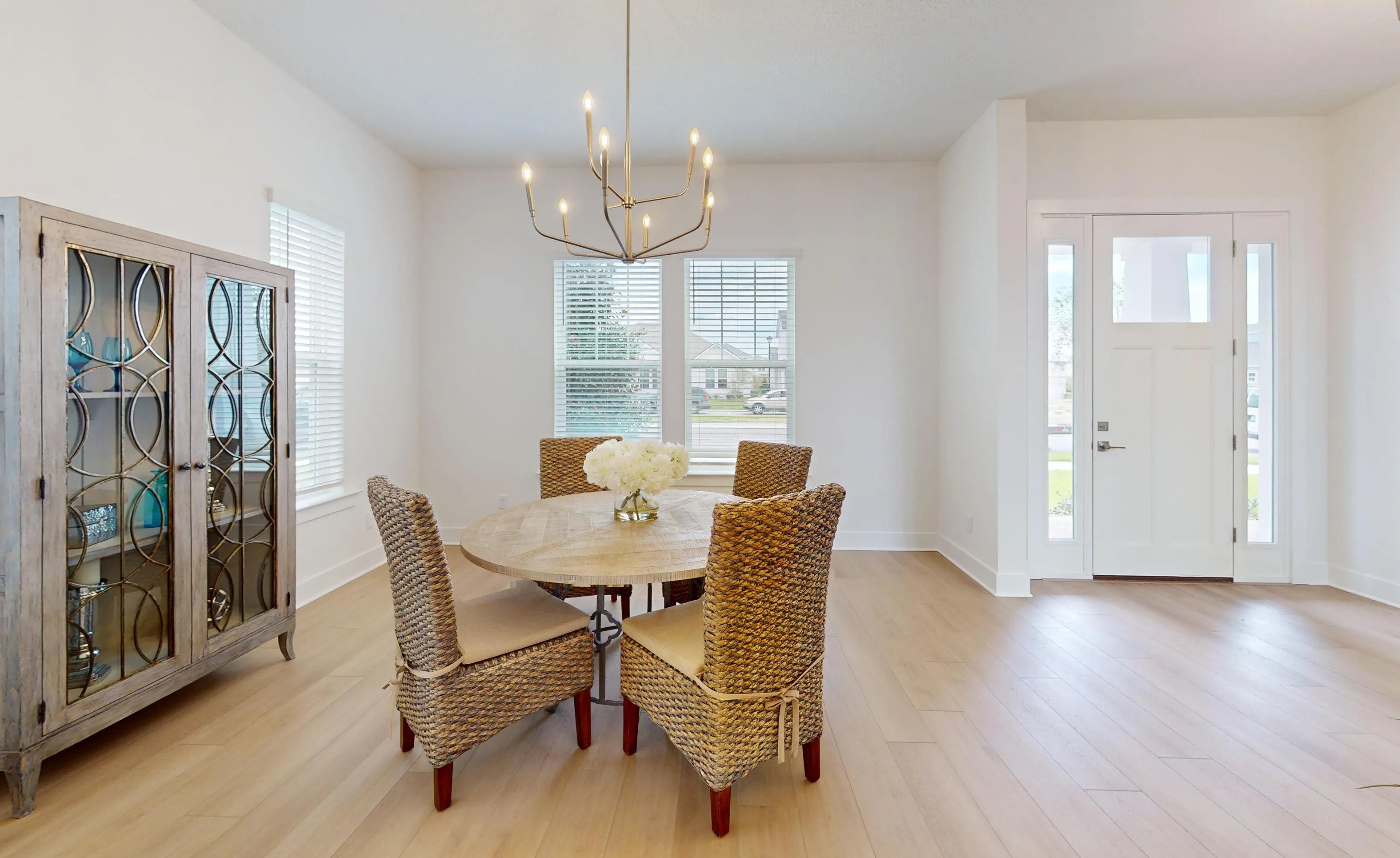 Braddock plan dining room featuring a round wooden table, four woven chairs, a metal chandelier, and a glass-front cabinet.