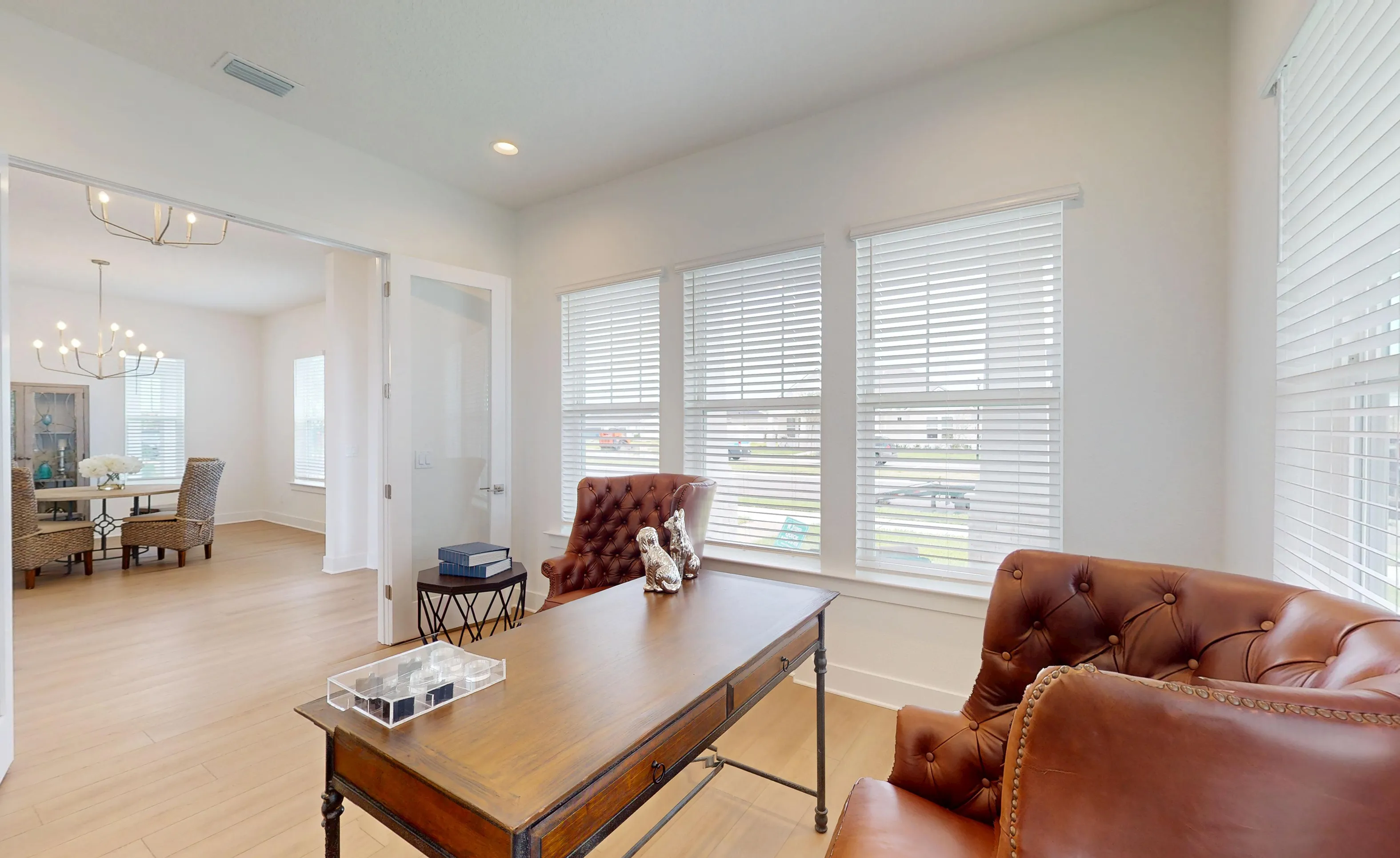 Home office in the Braddock plan with a wood desk, tufted leather chairs, large windows with blinds, and view of dining room.