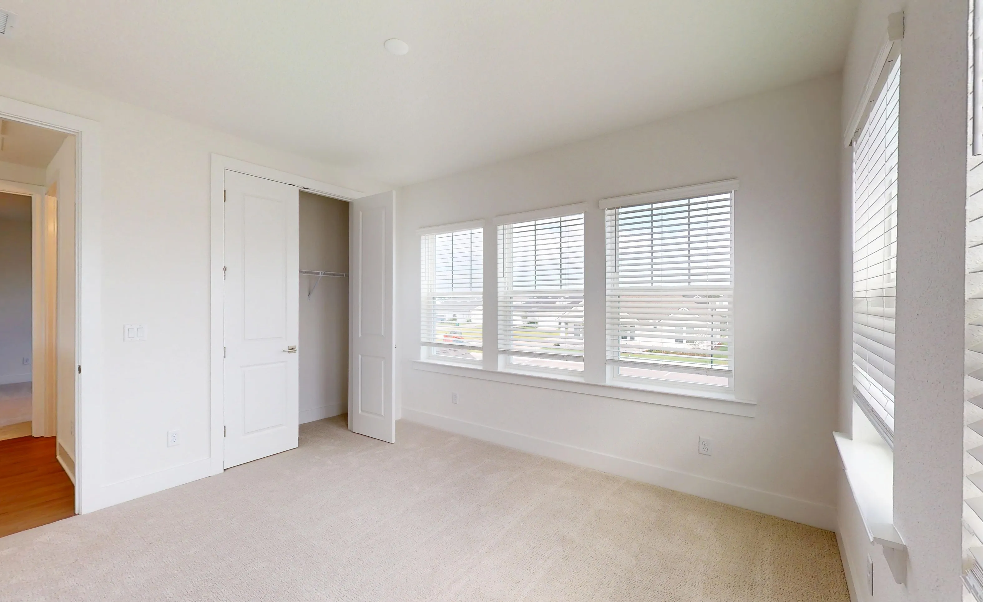Secondary bedroom in the Braddock plan with white walls, carpeted floors, an open closet, and multiple windows with blinds.