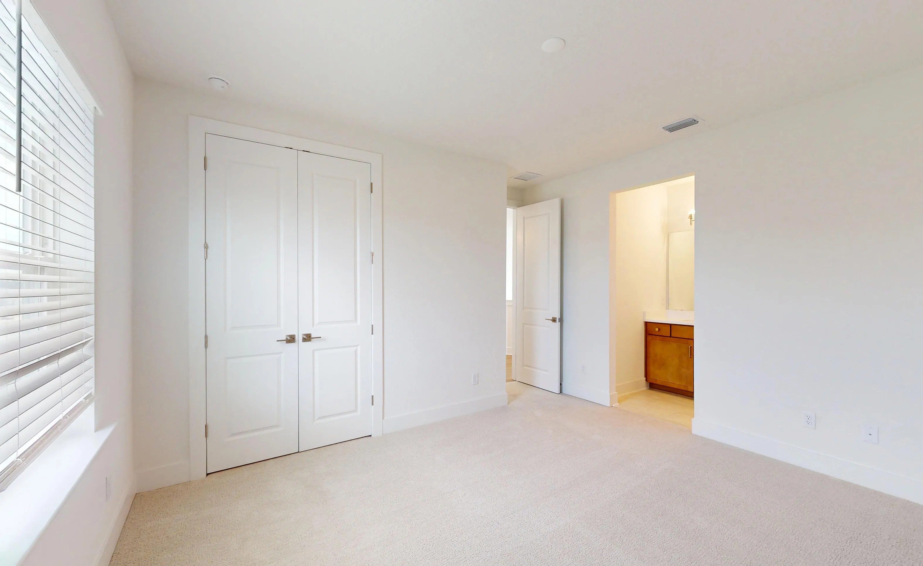 Secondary bedroom in Braddock plan with carpet, white double closet doors, and open doorway to an en-suite bathroom.