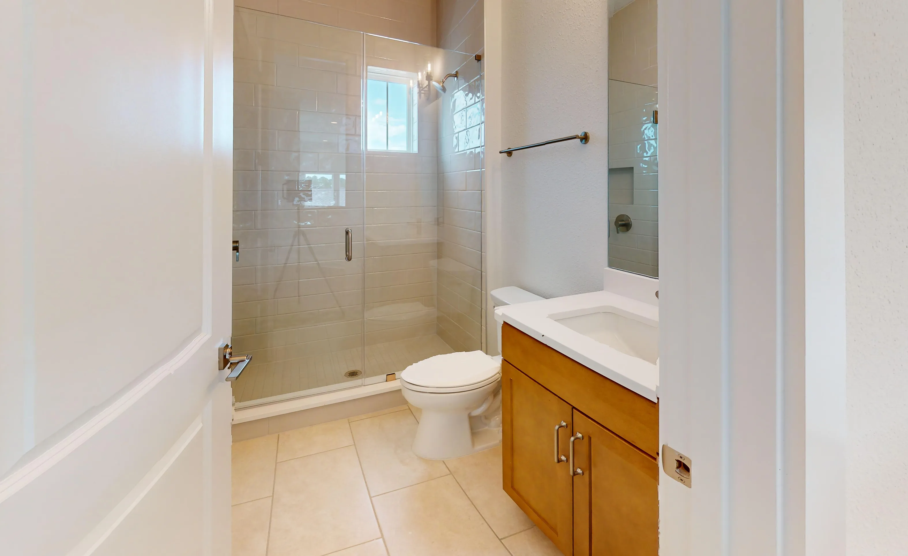 Secondary bath with a glass-enclosed shower, light wood vanity, white countertop, and tile flooring.