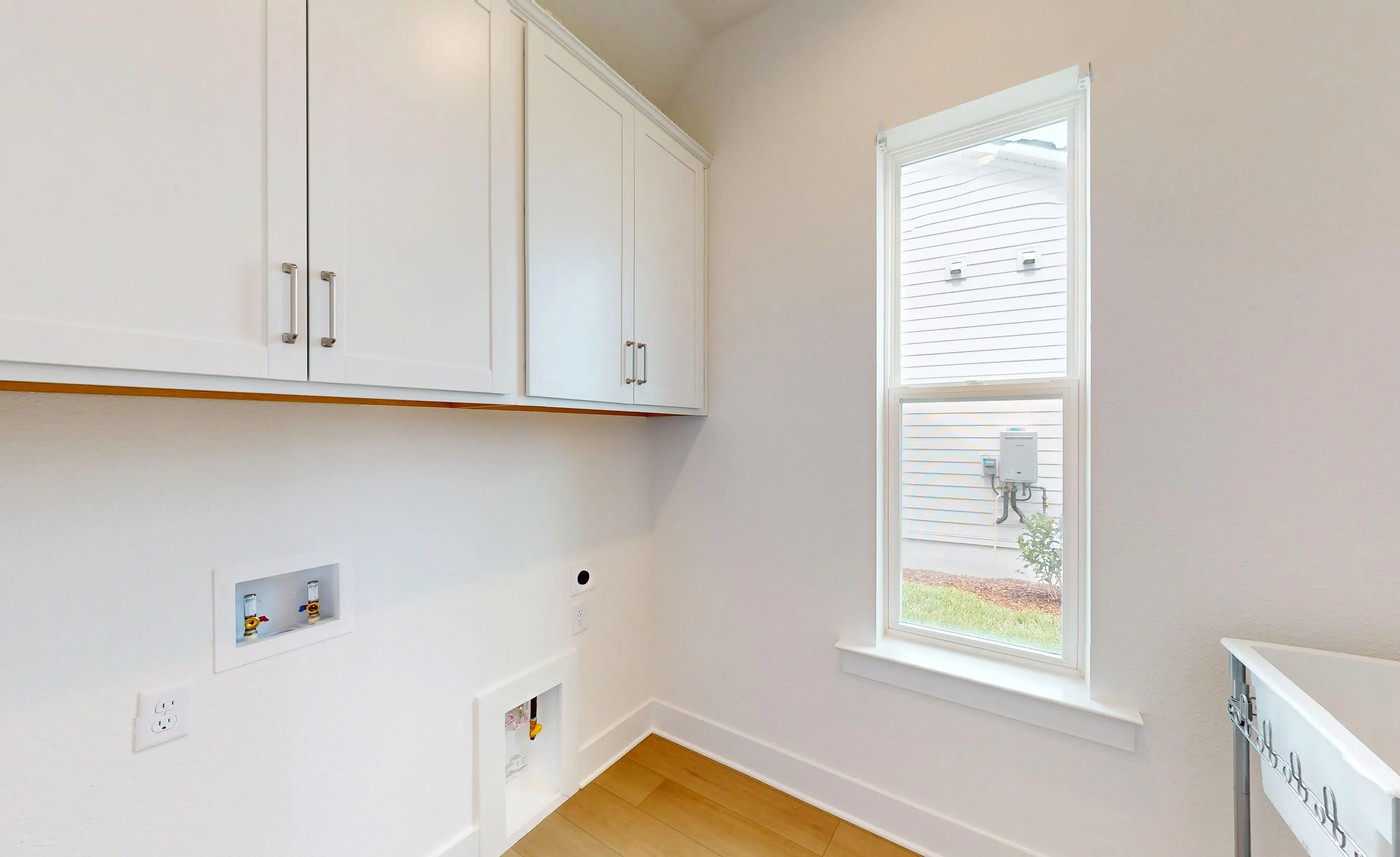 Laundry room with white cabinets, a window, and utility hookups for a washer and dryer on a wood floor.