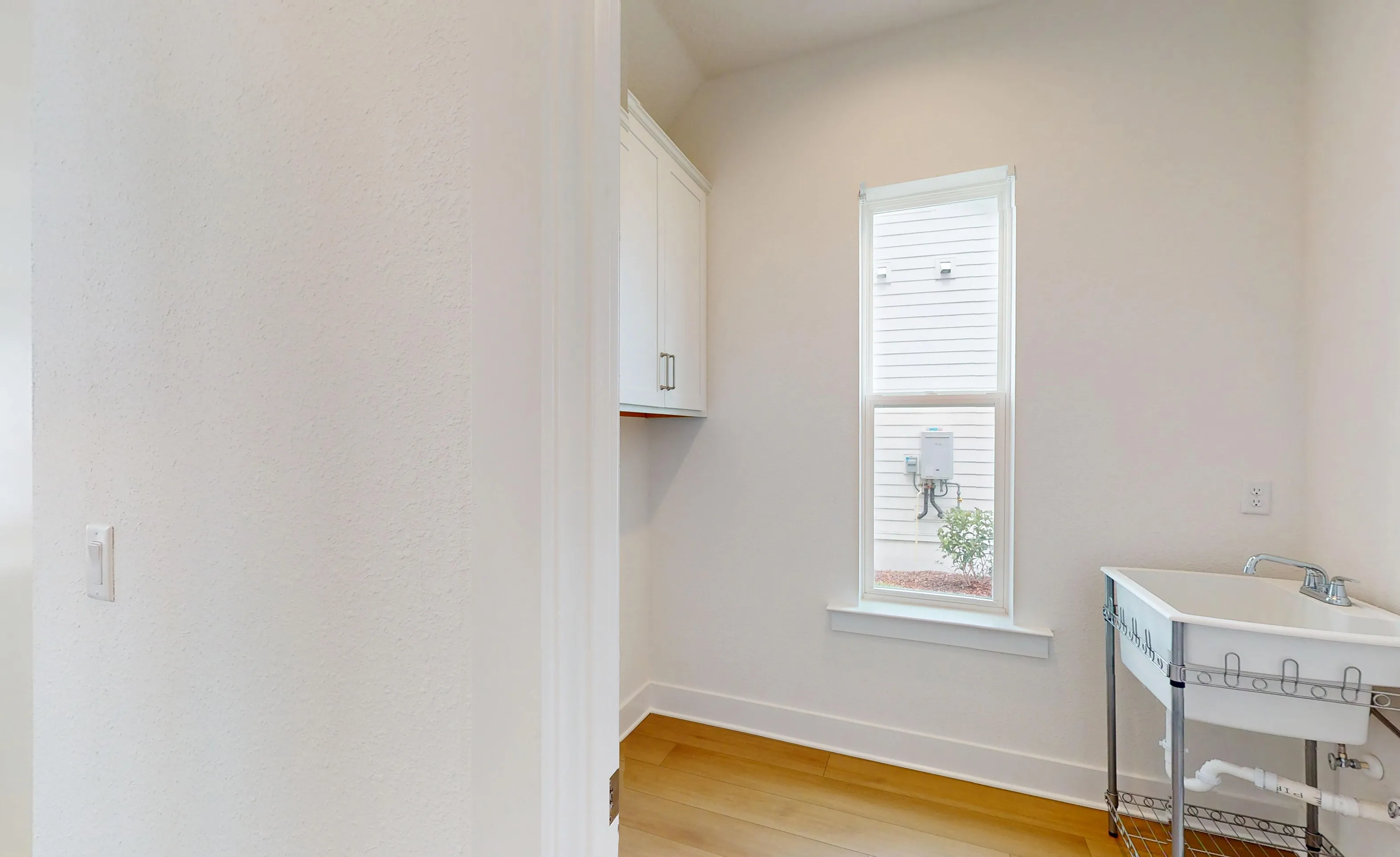 Laundry room in Braddock plan with white wall-mounted cabinets, a window, wood flooring, and a utility sink.