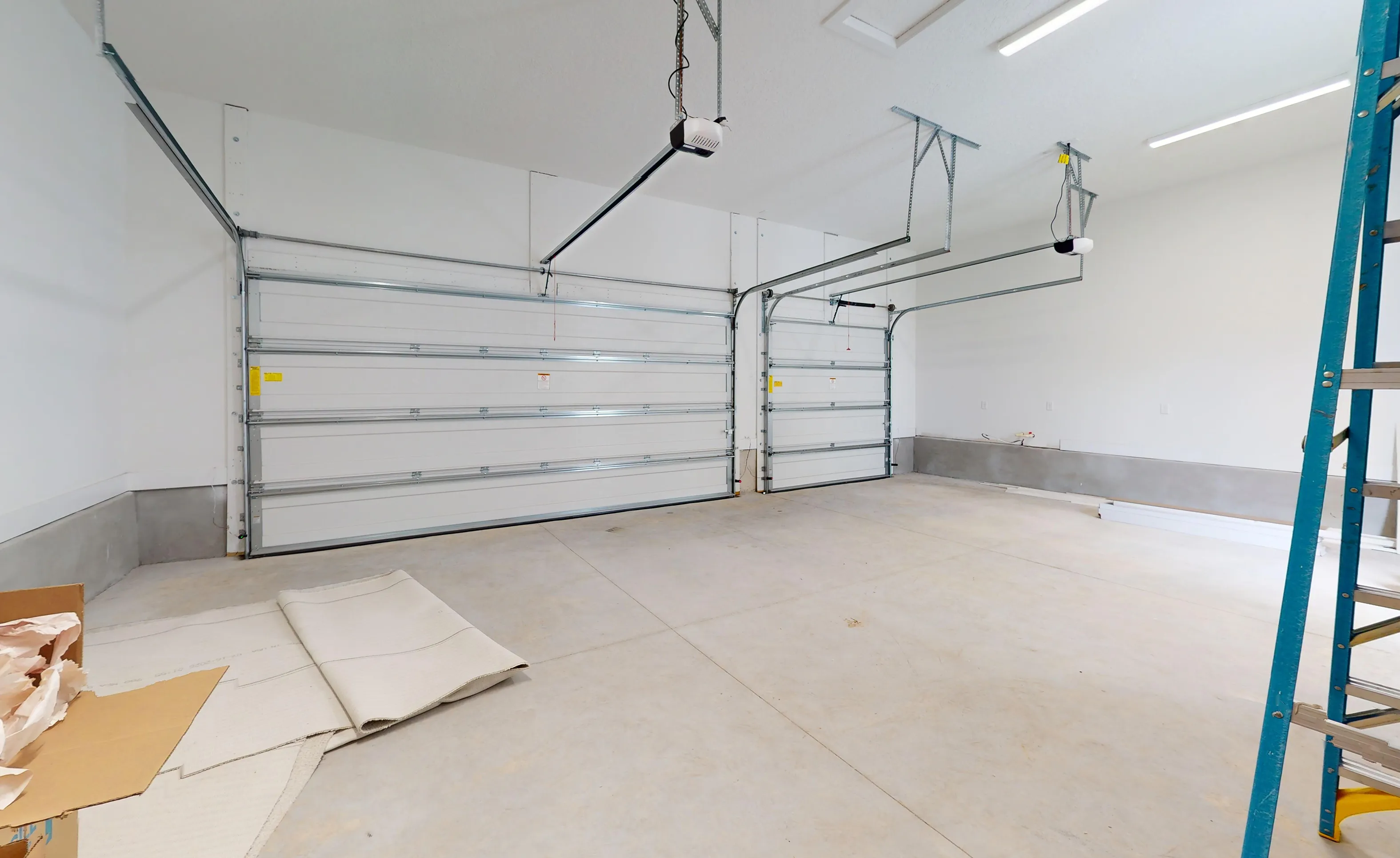 Empty two-car garage of the Braddock plan in Seven Pines with white walls, concrete floors, and two white garage doors.