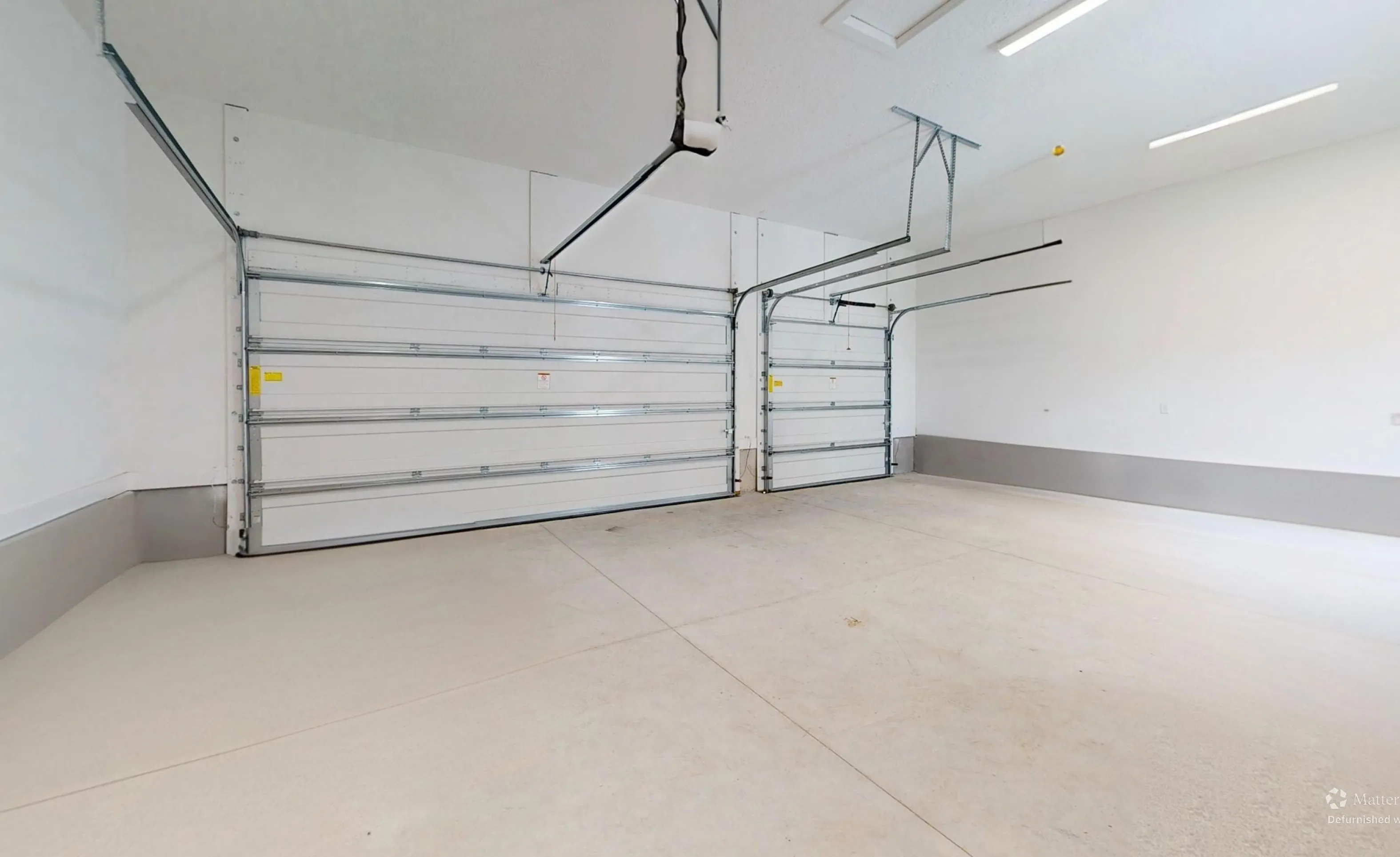 Empty multi-car garage in the Braddock plan with white walls, concrete floors, and two white metal garage doors.